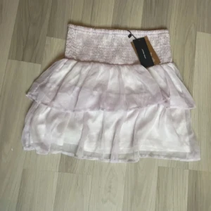 Ljuslila volangkjol - Supersöt ljuslila volngkjol med vita blommor från Vero Moda med bred smock i midjan och dubbla lager volanger. Helt ny med prislapp. Pris kan diskuteras💕