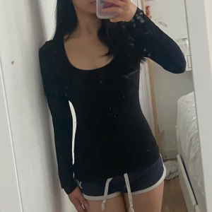 Svart långärmad topp med rund hals - En svart, tight långärmad topp med rundad, djup urringning. Sitter figurnära och har en enkel, stilren design som passar perfekt till jeans eller kjol. Materialet känns mjukt och stretchigt, vilket gör den bekväm att bära hela dagen.