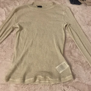 Glittrig meshtröja från Gina Tricot - Supersnygg glittrig meshtröja från Gina Tricot i ljusbeige med lång ärm och hög hals. Tröjan är tunn och transparent, perfekt att styla lager på lager eller med ett linne under. Ger en riktigt trendig vibe med sitt glittriga material.