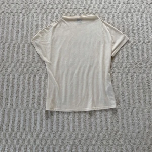 Beige t-shirt från Gina Tricot - Enkel och stilren beige t-shirt från Gina Tricot i mjukt material. T-shirten har korta ärmar och en rak passform. Det finns en liten fläck vid halsen (se sista bilden) som knappt är märkbar!