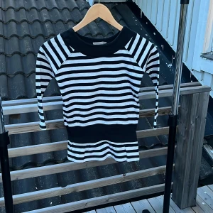 Randig svartvit tröja från KappAhl - Snygg svartvit randig tröja från KappAhl i 100% bomull. Tröjan har trekvartsärm, bred svart mudd vid hals och midja samt klassiska horisontella ränder. Perfekt för dig som gillar en enkel men stilren look.