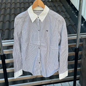 Randig skjorta från Esprit, stl 38 - Snygg skjorta från Esprit i vitt och blått med tunna ränder. Klassisk vit krage och vita manschetter ger en stilren kontrast. Skjortan har knappar framtill och lång ärm. Perfekt för dig som gillar en clean och tidlös look.