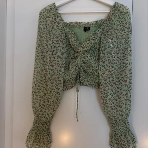 Grön blommig blus med snörning - Supersöt grön blommig blus från veromoda med långa puffärmar och smockade detaljer. Blusen har snörning framtill och volang vid ärmsluten. Perfekt för dig som gillar romantisk och trendig stil!