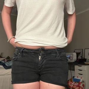 Svarta jeansshorts med snygga fickor - Low waist svarta jeansshorts med klassisk femficksdesign och kontrastsömmar på bakfickorna. Shortsen har låg midja och är tillverkade i stretchig denim för en bekväm passform. Perfekta för en avslappnad och cool look. De är storlek W29. 