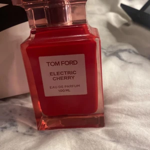 Tom Ford Electric Cherry 100ml parfym - 80/100% kvar i flaskan ,Tom Ford Electric Cherry Eau de Parfum i en snygg röd glasflaska på 100 ml. Flaskan har en lyxig, fyrkantig form med genomskinlig rödtonad kork. Doften är känd för sina fruktiga och sensuella körsbärsnoter, perfekt för dig som gillar unika och djärva parfymer.