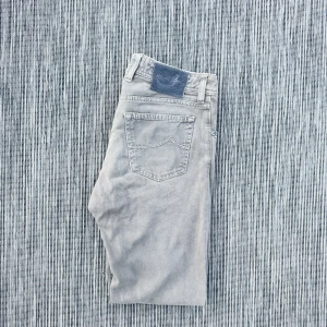 Jacob Cohen - Snygga gråa jeansbyxor från Jacob Cohen med klassisk femficksdesign och diskret logopatch bak i midjan. Byxorna har raka ben och är tillverkade i mjukt bomullsmaterial för en bekväm känsla. Perfekta för en stilren och avslappnad look.!AI BESKRVINING! Om ni vill ha fler bilder eller om ni har andra funderingar och frågor skriv.