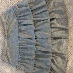 Grå volangkjol från Zara - Supersöt grå kjol från Zara med flera volanger. Kjolen är kort och har en mjuk, stretchig midja. Perfekt för dig som gillar en lekfull och trendig stil. Materialet är mjukt och bekvämt, passar till många olika outfits. Har inbyggda shorts