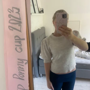 Beige stickad tröja med puffärm - Superfin beige stickad tröja med puffiga halvlånga ärmar och rund hals. Tröjan har en lite croppad passform och ribbade muddar vid ärmslut och halsringning. Perfekt för dig som gillar en enkel men trendig look. Från gina