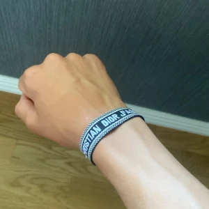 Christian Dior J'Adior armband blå - Snyggt vävt armband från Christian Dior i blått och vitt med texten 'J'Adior'. Justerbar knytning med tofsar i ändarna. Perfekt accessoar för att lyfta din outfit med en lyxig touch och cool streetkänsla.