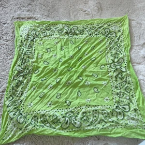 Limegrön bandana halsduk - Snygg limegrön bandana halsduk med klassiskt paisleymönster i svart och vitt. Fyrkantig form och tunn, mjuk bomull som är lätt att knyta runt halsen eller i håret. Perfekt accessoar för att ge din outfit en färgklick.