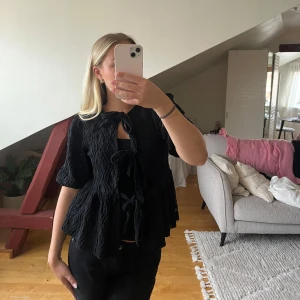 Svart blus med knyt och volang - Svart blus med korta puffärmar och flera knyt framtill. Jag har ett linne under på denna bilden! 