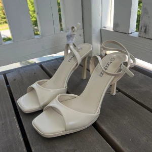 Krämvita klackar Boohoo - Snygga krämvita sandaler från Boohoo med hög klack och fyrkantig tå 💕. Helt ny köpta, endast vänster klack provad. Klack höjd: ca. 10cm. Har utbytbara knoppar under klacken som kan bytas ut (bild)