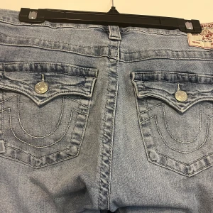 True Religion ljusblå bootcut jeans - Hej! Säljer dessa jeans från true religion, eftersom att de är för stora för mig. Jeansen är i storlek 32.  Byxorna köptes i oktober och har använts sparsamt. Byxorna har inga tydliga defekter som syns, däremot så är slutet av byxorna lite slitna, och det finns även små hål i midjebandet av säkerhetsnålar som ej syns. Skriv gärna till mig för mer info och bilder. 🤗