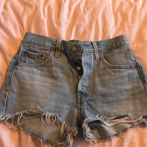 Levi's ljusblå jeansshorts med fransar - Ljusblå jeansshorts från Levi's med hög midja, råa fransade kanter och klassiska fem fickor. Knappar framtill och Levi's-lapp bak. Perfekta för sommaren och ger en avslappnad vibe.