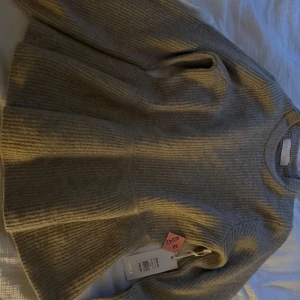 Beige stickad tröja från SAMSA - Supermysig beige stickad klänning från SAMSA Collection i ribbat material. Klänningen har rund halsringning, lång ärm och en lätt utställd kjol. Perfekt för dig som gillar en enkel men snygg look med lite volym nertill.