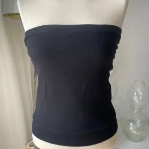Svart bandeau tubtopp i bomull - Enkel och stilren svart bandeau tubtopp i mjuk bomull med elastisk kant upptill för att sitta på plats. Perfekt att styla med jeans eller kjol för en clean look. Ärmlös och axelbandslös design som ger en snygg siluett. Dubbla tyger vid bröstet med gummi kant 