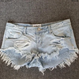 Ljusblåa jeansshorts med fransar - Snygga ljusblå jeansshorts från One Teaspoon med slitna detaljer och fransig kant. Klassisk femficksmodell med låg midja och råa kanter för en cool, avslappnad vibe. Perfekta för sommardagar när du vill sticka ut lite extra.