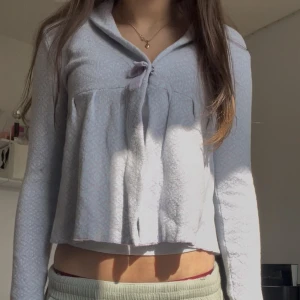 Ljuslila kofta med rosett och mönster - Supersöt ljuslila kofta med diskret mönster och en liten rosett framtill i storlek xs och nästan aldrig använd