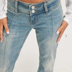 Lågmidjade blå bootcut jeans - Snygga lågmidjade jeans i ljusblå tvätt med bootcut-snitt och två knappar framtill. Jeansen har markerade sömmar längs benen och klassiska fickor. Perfekta för dig som gillar retrovibbar och vill ha en cool siluett.