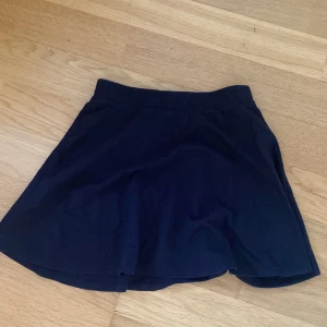 Svart kortkjol från Kappahl - Enkel och stilren svart kortkjol från Kappahl. Kjolen har en lätt utställd passform och resår i midjan för extra komfort. Perfekt att matcha med en cool t-shirt eller hoodie.