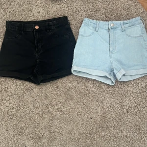 Svarta & ljusblå jeansshorts, hög midja - Två par jeansshorts med hög midja, ett par i svart och ett par i ljusblått. Båda har klassisk femficksdesign, knapp och dragkedja framtill samt uppvikta benslut. Perfekta för sommarens chill och häng. Shortsen har ett lagat hål på framsidan av de svarta jeansshortsen och en fläck på en av bakfickorna på de ljusblå! Storlek 152, ca 11-12 år. Säljer pga för små för mig!
