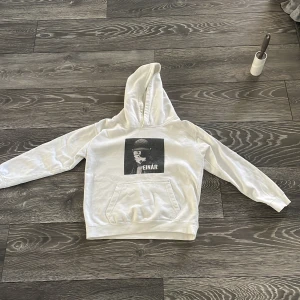 Vit Einár hoodie med tryck - Vit hoodie med stor svartvit Einár-tryck på bröstet och texten 'Nu vi skiner' på ryggen. Tröjan har huva, magficka och långa ärmar. Perfekt för dig som gillar svensk hiphop och vill ha en unik streetstyle-look.