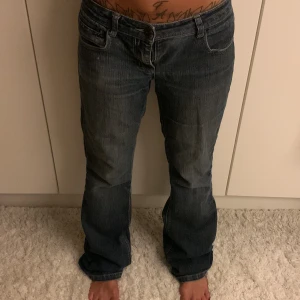 Blå bootcut jeans med broderade fickor - Säljer ett par blå jeans med bootcut passform och snygga broderade bakfickor med knappdetalj. Jeansen har klassisk femficksdesign, låg midja och är tillverkade i jeansmaterial med kontrastsömmar. Perfekt för dig som gillar en avslappnad och cool stil. The zipper is broken