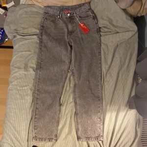 Levi's 501 grå jeans, hög midja - Säljer ett par Levi's 501 jeans i grå tvätt med klassisk femficksdesign och knappgylf. Modellen har hög midja och raka ben med normal passform. Jeansen är tillverkade i slitstark denim och har en snygg vintage vibe. Perfekt för dig som gillar tidlös stil. Jeansen är 158-164cm långa