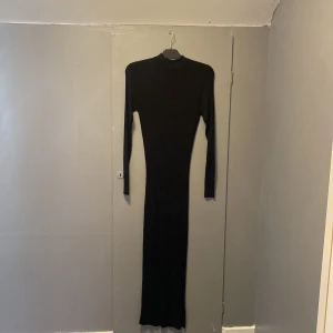 Svart långklänning med polokrage - Snygg svart långklänning med polokrage och långärmade ärmar. Klänningen har en slim passform som framhäver figuren och är helt enfärgad utan detaljer. Perfekt för dig som gillar minimalistisk och stilren design.