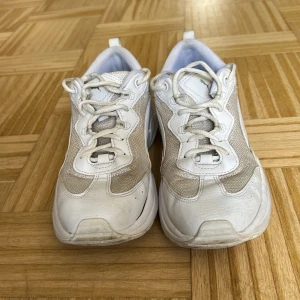 Vita sneakers från Puma SoftFoam - Säljer ett par vita Puma sneakers med SoftFoam+ innersula för extra komfort. Skorna har meshpaneler på sidorna, detaljer i syntet och skinn, samt snörning framtill. Rund tå och platt sula ger en klassisk look. Perfekt för dig som gillar stilrena och sportiga sneakers.
