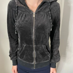 Svart velour hoodie från Peak Performance - Mjuk och skön svart hoodie i velour från Peak Performance med broderad logga i lila på ärmen. Tröjan har huva med snörning, dragkedja framtill och två fickor. Ribbad mudd vid ärmslut