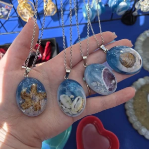 Blå halsband med strandtema - Unika halsband med oval blå hängare fylld med stranddetaljer som snäckor, sjöstjärna och små stenar. Hängarna har en cool havsinspirerad look och sitter på silverfärgade kedjor. Perfekt för dig som älskar strandvibbar och vill sticka ut med något annorlunda. Handgjorda med kärlek, skriv vilken du vill ha vid köp.