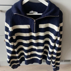 Randig stickad tröja från Zara - Säljer en snygg stickad tröja från Zara i marinblått och vitt med breda ränder. Tröjan har lång ärm, krage och en half zip-dragkedja framtill. Perfekt för dig nu till hösten. Mjuk och skön kvalitet som håller värmen! 