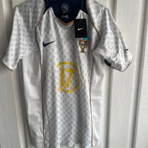 Portugal C. Ronaldo 17 Nike fotbollströja - Snygg Portugal fotbollströja från Nike med C. Ronaldo och nummer 17 i gult på ryggen och bröstet. Tröjan är vit med ljusgrått mönster, korta ärmar och guldfärgade detaljer längs kanterna. UEFA Fair Play-märke på ärmen och Portugal-emblem på bröstet. Perfekt för fans!
