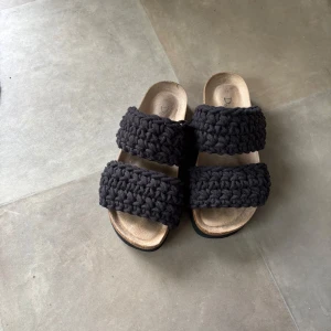 Svarta stickade sandaler från Duffy - Unika sandaler från Duffy med två breda, stickade svarta band över foten. Sulan är beige och ergonomiskt formad för extra komfort, medan yttersulan är svart och räfflad för bra grepp. Perfekt för dig som gillar en chill och trendig stil.