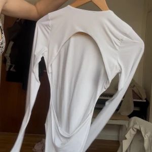 Vit långärmad body med öppen rygg - Säljer en vit långärmad body med en riktigt snygg och stor öppning i ryggen. Toppen har en slim passform och är tillverkad i mjukt syntetmaterial som sitter skönt mot kroppen. Perfekt för dig som gillar att sticka ut med coola detaljer.