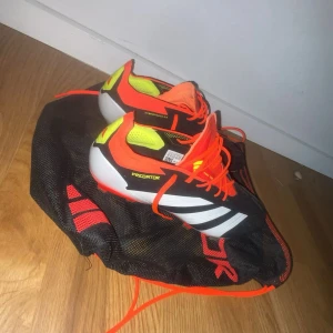 Adidas Predator fotbollsskor svart/röd - Säljer ett par Adidas Predator fotbollsskor med snygg design i svart, rött och neon-gult. Skorna har snörning, låg profil och mönstrad sula med dobbar för gräsplan. Ovandelen är tillverkad i syntetmaterial med Hybridtouch 2.0 för extra komfort och kontroll. Perfekt för dig som vill sticka ut på planen. Aldrig använda!!!