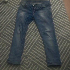 Blå jeans från Nudie Jeans Co - Säljer ett par snygga blå jeans från Nudie Jeans Co, tillverkade i ekologisk bomull. Jeansen har klassisk femficksdesign, raka ben och subtila slitningar för en cool look. Passar dig som gillar stilrena och tidlösa jeans med schysst passform. PRIS KAN DISKUTERAS 