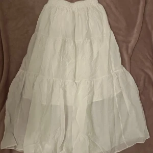 Vit långkjol med volanger - Säljer en superfin vit långkjol med flera volanger och elastisk midja. Den är luftig och lätt och passar till somriga/våriga tillfällen. Bra skick!!