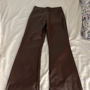 Bruna bootcut byxor i skinnimitation H&M - Snygga bruna bootcut-byxor från H&M i skinnimitation. De har en hög midja och ett stilrent, slätt utseende utan synliga fickor eller detaljer. Perfekta för dig som vill ha en trendig och edgy look med lite extra attityd.