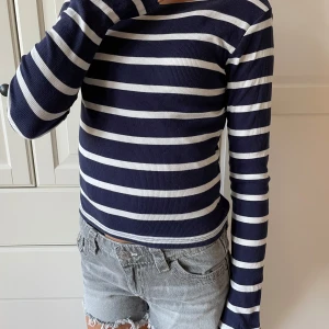 Randig långärmad tröja från Kappahl - Säljer en marinblå och vit långärmad tröja från Kappahl i ribbad bomull. Tröjan har horisontella ränder och en klassisk, lite tight passform som sitter snyggt. Perfekt till jeans eller shorts för en chill look.