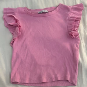Rosa volangtopp från Zara - Supersöt rosa topp från Zara i ribbad bomull med volangdetaljer på axlarna. Modellen är ärmlös och har en rund halsringning. Säljer då den inte riktigt passar mig längre! Storlek S! OBS, katt finns i hemmet!