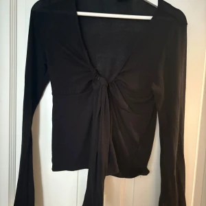 Svart omlottopp med knyt från Gina Tricot - Svart omlottopp från Gina Tricot i storlek M. Toppen har lång ärm och en knytning framtill. 