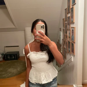 Vit tubtopp med volang - Säljer en söt vit tubtopp med smockad överdel och volang nedtill. Perfekt till jeansshorts eller kjol för en chill look.