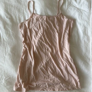 Ljusrosa linnetopp med smala axelband - Säljer en enkel och stilren ljusrosa linnetopp med smala axelband. Toppen är ärmlös och har en rak, slim passform som sitter snyggt mot kroppen. Perfekt att matcha med jeans eller shorts för en chill look.