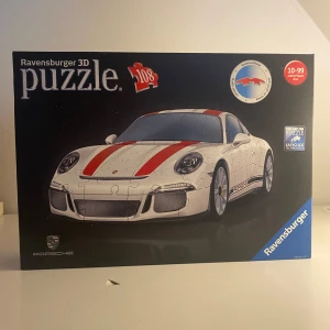 Ravensburger 3D Puzzle Porsche 911 R - Bygg din egen Porsche 911 R med detta 3D-pussel från Ravensburger! Med 108 bitar och cool design är det perfekt för dig som gillar bilar och utmaningar. Passar både ungdomar och vuxna som vill ha en unik modell att visa upp.