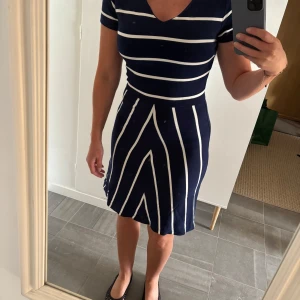 Klänning GANT - Klänning från GANT i marinblått med vita ränder. Klänningen har v-ringad hals, korta ärmar och ett figurnära liv med utställd kjol. Tillverkad i mjuk bomull. 