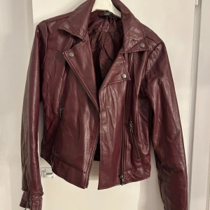 Vinröd skinnjacka med dragkedjor - Snygg vinröd skinnjacka med defekter längst ner på ärmen, storlek s💕