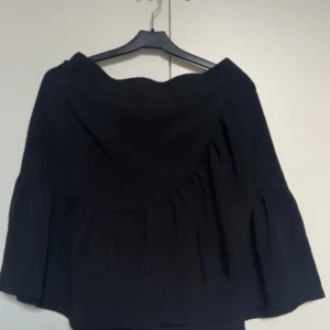 Svart volangkjol från Lindex - Svart kjol från Lindex i storlek M. Kjolen har en volangdetalj och är kort i modellen. Den har en mjuk och flowy känsla med resår i midjan för skön passform. Perfekt att matcha med en cool topp och boots.