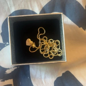 Guldigt halsband med hjärthänge - Snyggt halsband i guld med ett hjärthänge dekorerat med glittrande stenar. Kedjan har en klassisk design och hängsmycket ger en romantisk vibe. Perfekt för dig som gillar detaljer och vill sticka ut lite extra. Äkta 18 rent guld! Köptes för 4000 säljer för 3000